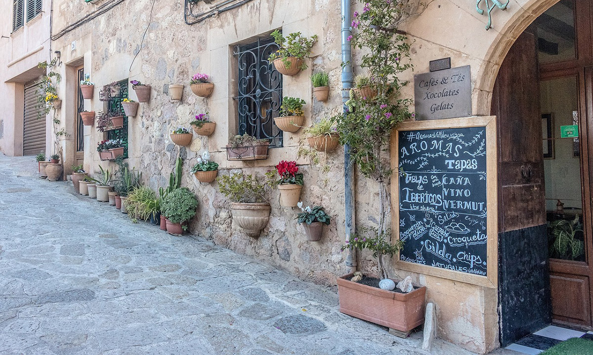 altes Steinhaus auf Mallorca mit vielen bunten Blumentoepfen und einem Cafe darinne