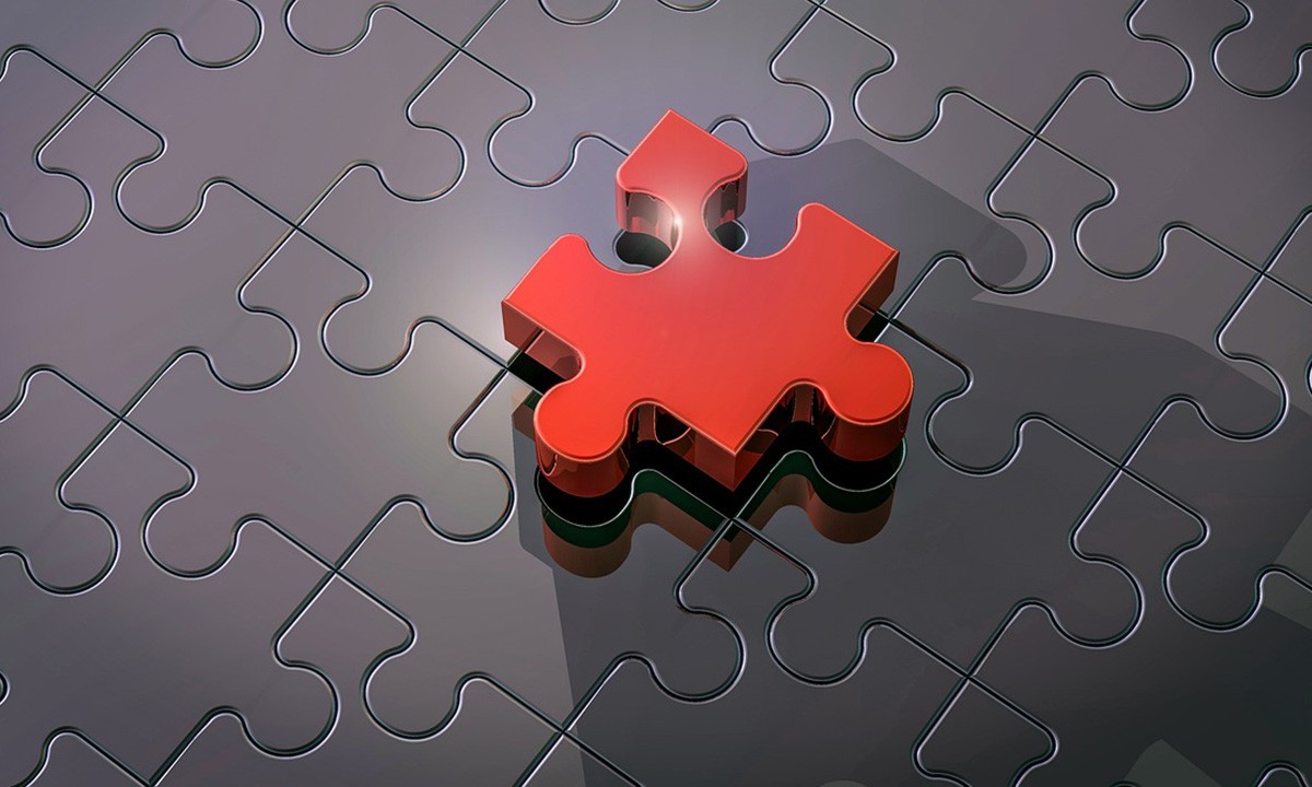 Symbolbild: Ein rotes Puzzleteil fuellt die letzte Luecke in einem ansonsten vollstaendigen grauen Puzzle